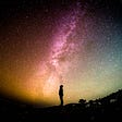 silhouette of a person looking up at the milky way galaxy at night