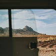 A view of a field in Africa, with mountains in the background. Photo was taken from inside a vehicle.