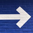 A white arrow pointing to the right on a dark blue wall.