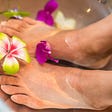 Photo of a woman with her feet soaking in a basin of water with flowers.