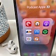 Picture of podcast apps on phone screen and headphones in background