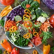 a huge bowl of vibrant and colorful vegetables cut up with a large for resting on top