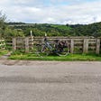 Bike leaning on fence by side of road with fields and hills in the distance