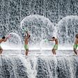 Four men are standing in what appears to be a waterfall, splashing each other.