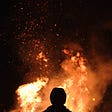 A figure standing in front of a huge fire.