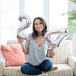 Brunette woman sitting on a white couch with silver “24” balloons for her birthday