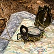 An image of a map in plastic lying on the ground and an old-fashioned compass resting on the map.