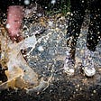 Two young people stand in a puddle, muddy water splashing up around them.