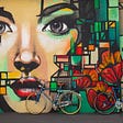 A mural featuring a woman’s face and geometric shapes around her that also feature flowers. There are bikes in front of the mural.