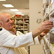A pharmacist retreives a patient’s prescription from a pharmacy shelf.