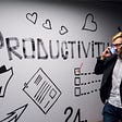 A blonde man talks on the phone while passing a wall that says “PRODUCTIVITY”