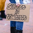 Person holding sign that says “Silence is Violence”