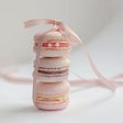 Pink macaroons stand in a column and tied with a pink ribbon and bow against a wooden background.