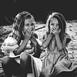 two little girls sharing a secret and laughing