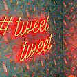 Neon sign on a wallpapered wall reads “# tweet tweet”