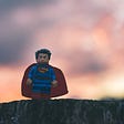 A LEGO Superman figurine looking badass straight at us, with sunset colors in the background and him standing on a tree stump watching.