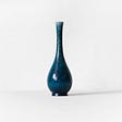 against the white backround we see a blue vase which is narrow at the top and wide at the bottom , its symmetrical .the light hits blue vase and a shadow appears on right side of the blue thin vase