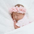 New born baby girl lying between white sheets with pink bow in her hair.