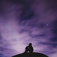 A person sits looking upwards, silhouetted against a starry, purple sky