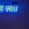 Blue neon lights saying “Work Harder.”