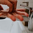 A man washing his hands thoroughly in running water at a white sink