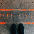 welcome written in orange letters on the ground beside black shoes