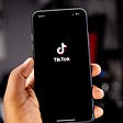 A hand holding a phone with the TikTok logo at the center
