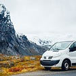 White van with snowy mountains and grass in the background