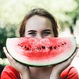 Woman with a large quarter slice of watermelon to her face, taking the shape of a Summer smile