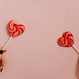 Two heart shaped lollipops held against a pink background