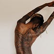 the image is that of a black male posing. His back to facing the camera and is adored with a large tattoo. I do not know of what. It looks like some geometric shapes. The artwork continues up his right arm.