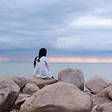 Woman sitting on a rock, looking out over the ocean.