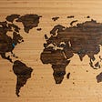 An image of a wooden world map with pins on it.
