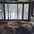 Comfortable bed overlooking a window with snowy forrest views.