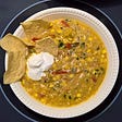Corn, Squash, and Tomatillo Soup garnished with tortilla chips and sour cream.