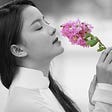 Asian girl in black and white, wearing a traditional Ao Dai dress and smelling a colored flower.