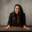 Headshot of Vanessa in yellow shirt with black blazer at a wooden table