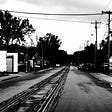 Black and white picture taken of rail tracks in the middle of small city