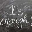 A grey chalkboard with the phrase “it’s enough!” hand-written with a white chalk