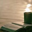 An open book and a mug of hot beverage, by the sea