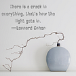 light grey background with grey vase and one long bending branch. Quote “There is a crack in everything, that’s how the light gets in. — Leonard Cohen” How the Wabi-Sabi Lifestyle Can Teach You to Embrace Imperfection by Nancy Blackman. imperfection, wabi-sabi, kintsugi