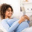 A pregnant woman rests on the sofa while using an app on her mobile phone