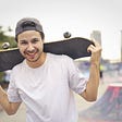 Smiling man with a reversed cap with a skateboard on his shoulders