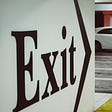 Black large sign stating “EXIT” on a white wall in a parking garage