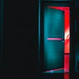An illuminated, ajar door at the end of a dark hallway