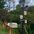 A mailbox at the side of the road. One has numbers on it. Another is labelled taxes and bills. Others are equally silly. Way high up is Air Mail.