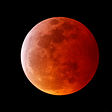An orange, reddish moon against a black sky with a smattering of stars.