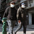 Two men walk together down the street with COVID-19 masks on.
