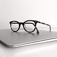 Pair of clear glasses resting on a closed Mac laptop