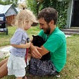 A young man and his daughter relate to a young black cat.